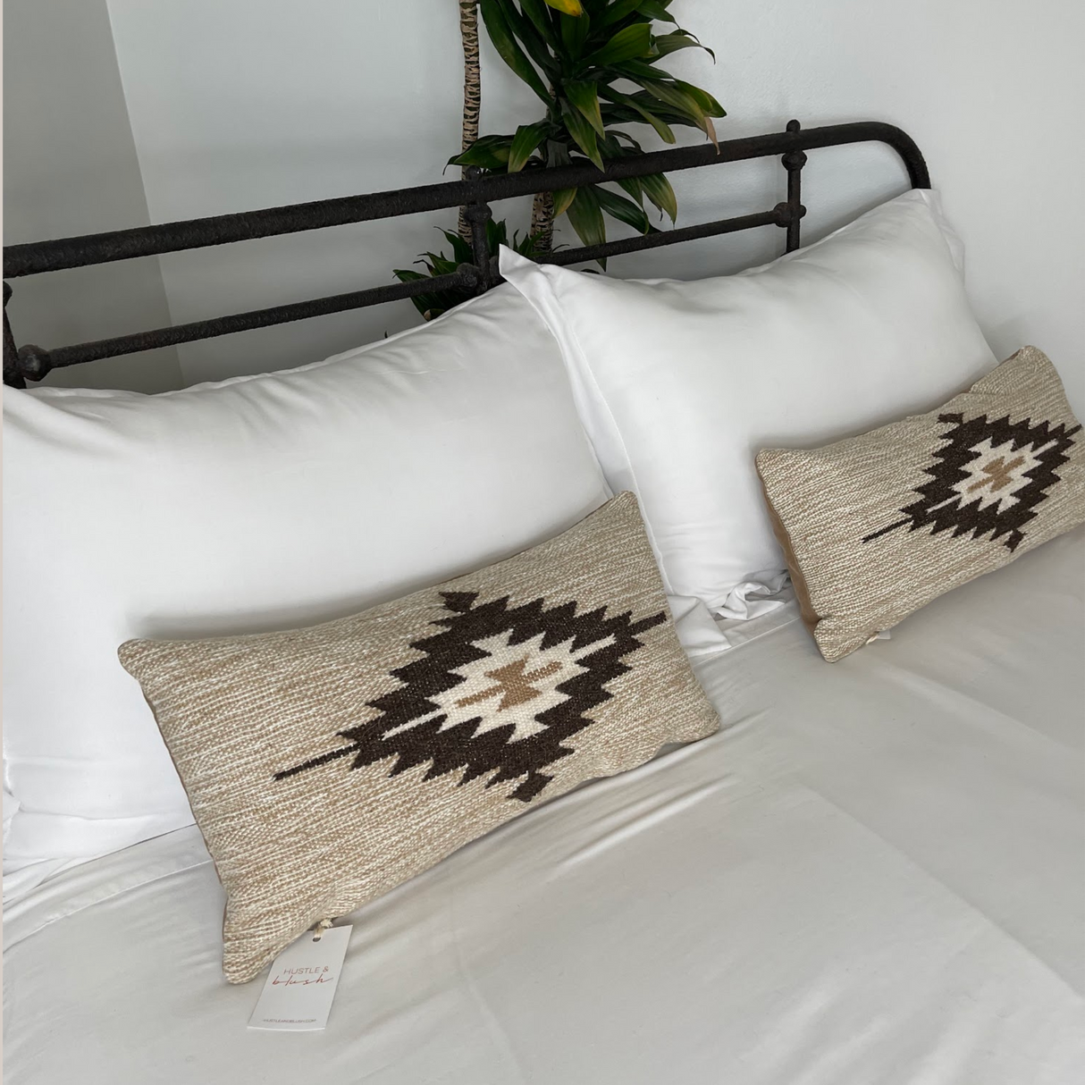 A neatly made bed with white linens is accented by two Handwoven Chitki (Crisp) Pillows, showcasing beige tones and black-and-white geometric patterns.
