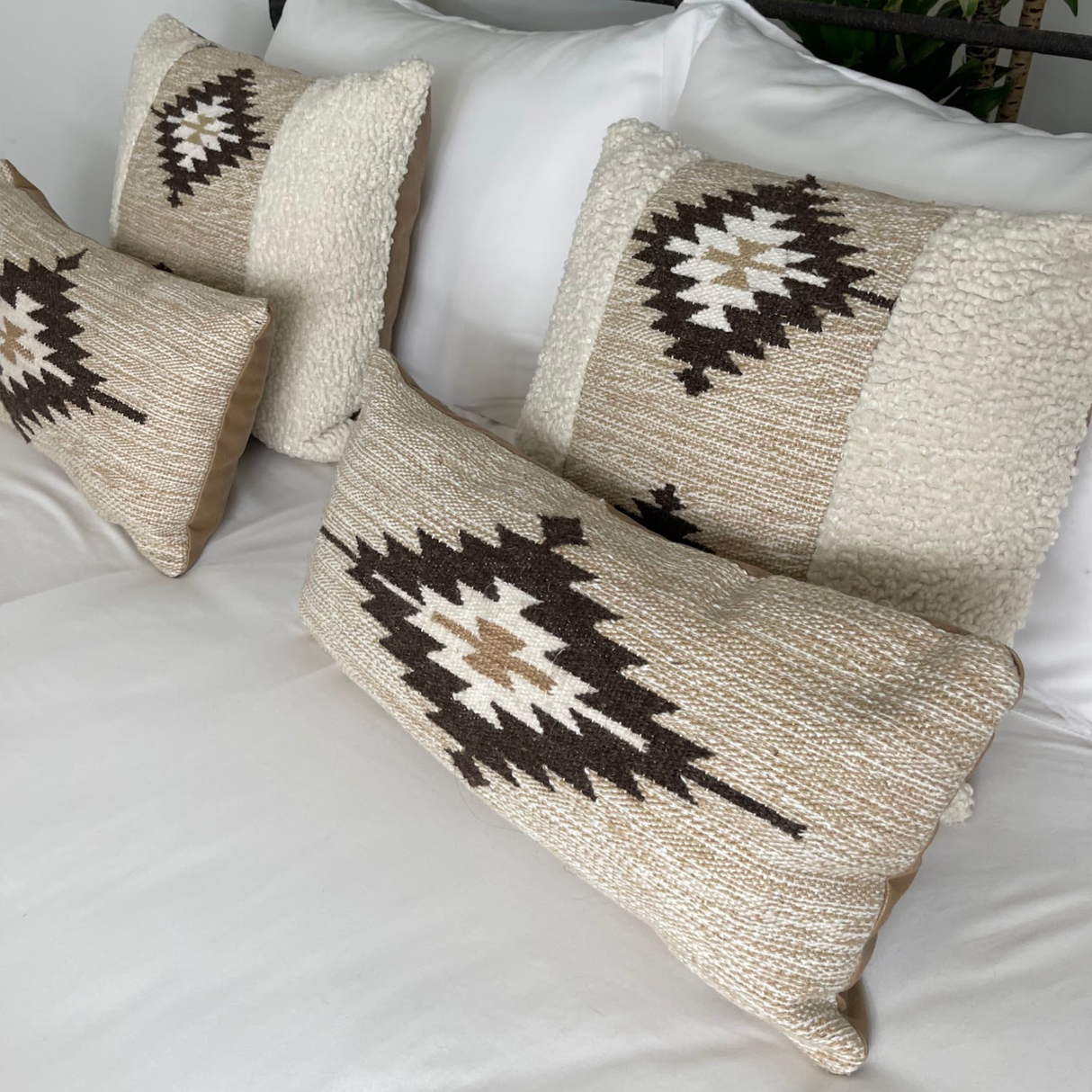 The Handwoven Chitki (Crisp) Pillow, featuring a geometric pattern, is styled alongside two other decorative pillows on a neatly made white bed.