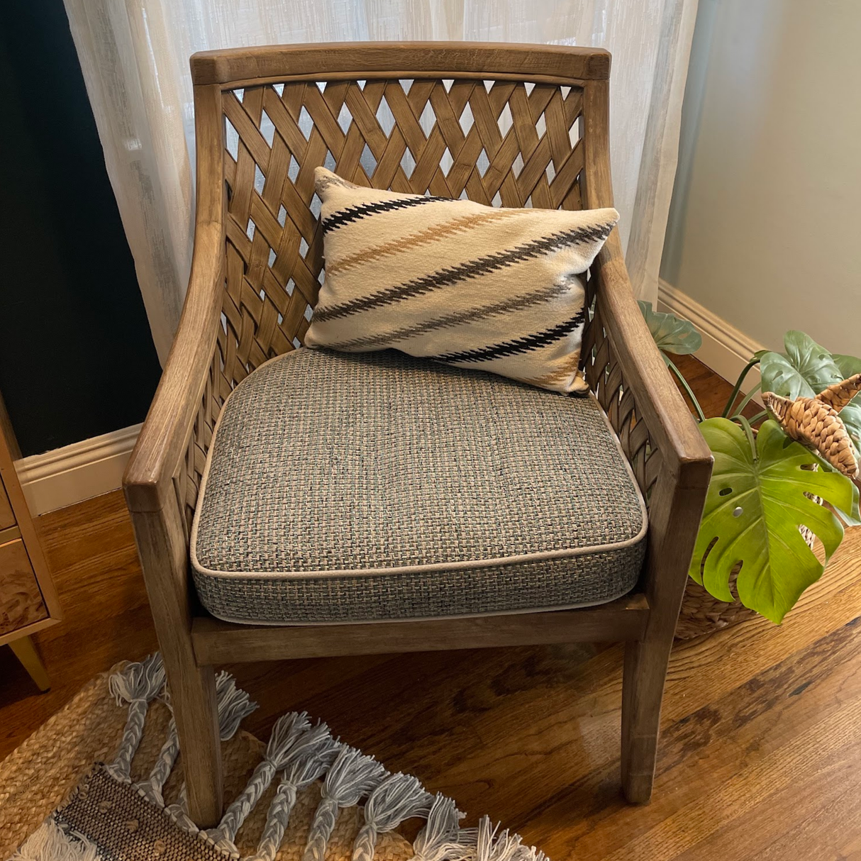 Wooden chair with a woven back, patterned cushion, and a Handwoven Promin (Beam) Wool Pillow beside a plant on a hardwood floor.