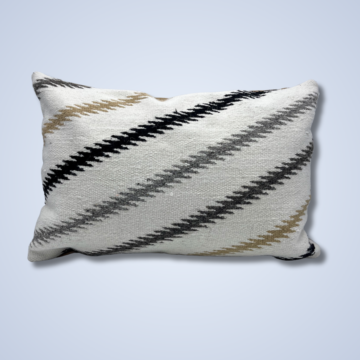 The Handwoven Promin (Beam) Wool Pillow is a rectangular decorative pillow with diagonal black, gray, and beige zigzag stripes on a light blue background.