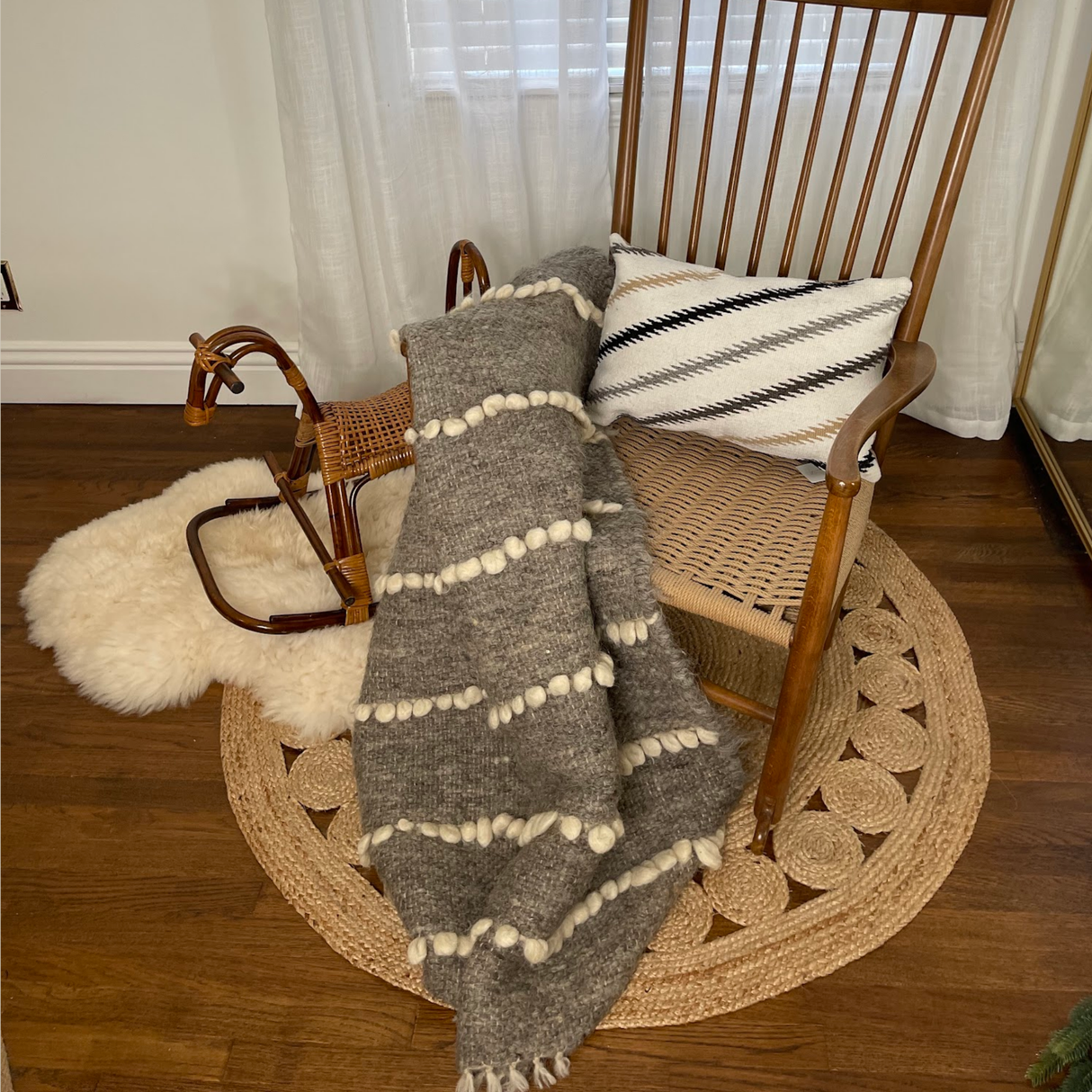 Wooden rocking chair with a Handwoven Promin (Beam) Wool Pillow and gray pompom blanket, next to a wooden rocking horse on a rug.