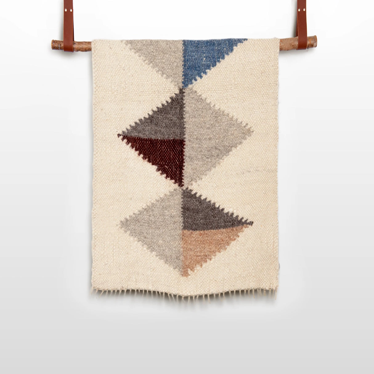 The Harmonia A Wool Statement Throw / Baby Blanket features woven geometric triangles in blue, grey, brown, and beige on a wooden rod for a cozy, stylish accent.