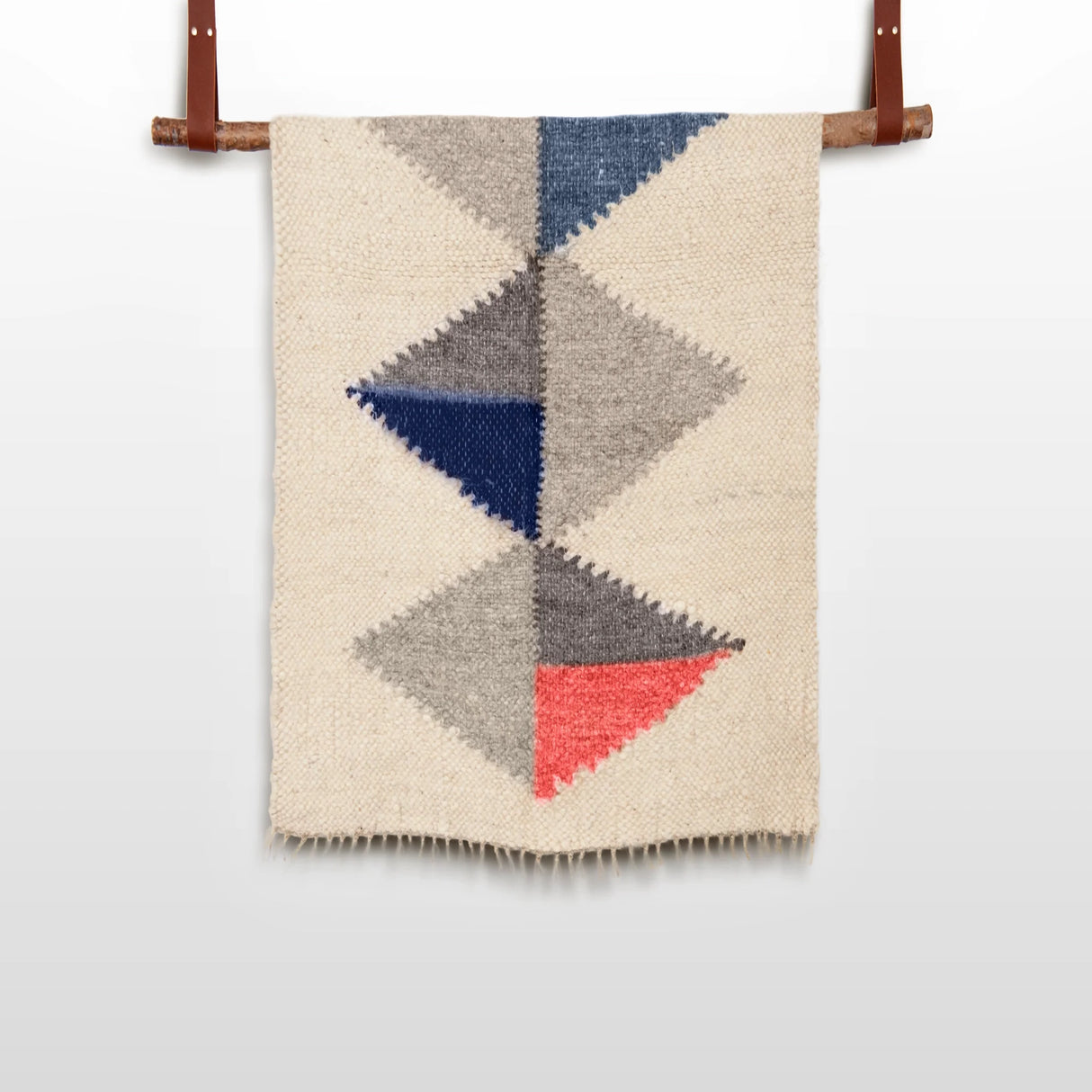 The Harmonia B (Harmony) Wool Statement Throw / Baby Blanket features colored triangles in blue, gray, and coral on a cream background, inspired by modern art blanket designs and displayed on a wooden rod.