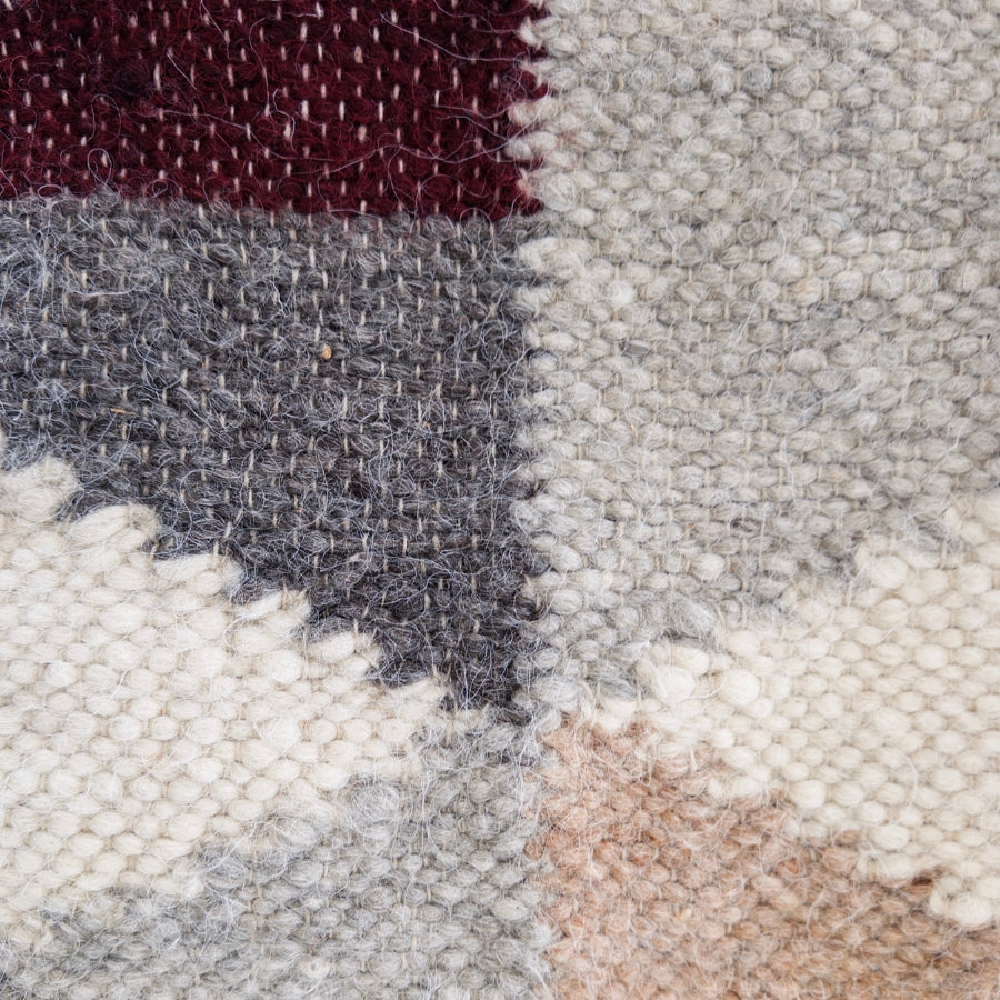Close-up of the Harmonia A (Harmony) Wool Statement Throw / Baby Blanket, featuring a geometric pattern with maroon, gray, white, and beige wool yarn blocks.