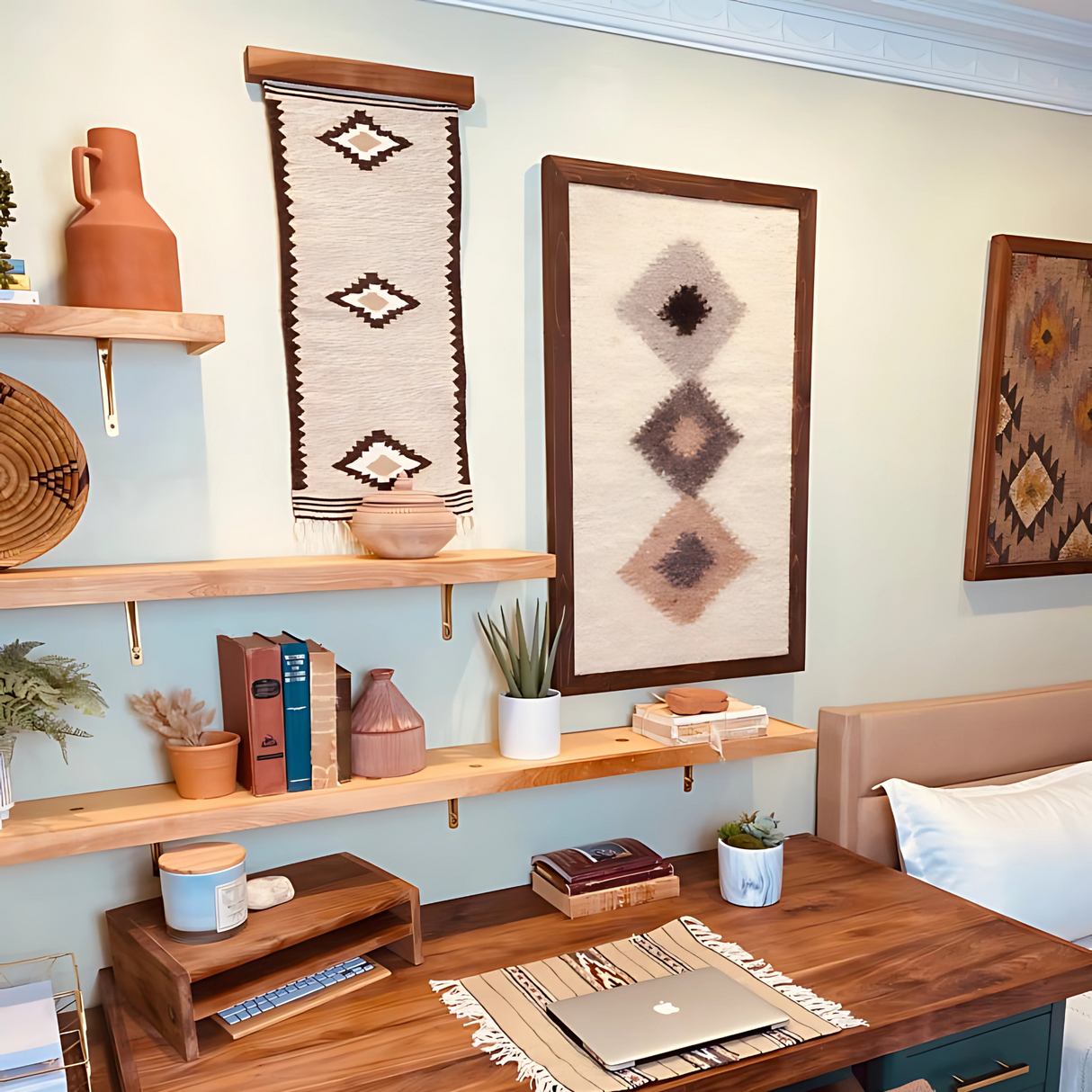A cozy workspace with wooden shelves, pottery, books, plants, and Harny (Beautiful) Wool Framed Wall Art in a cedar frame above a desk with a laptop.