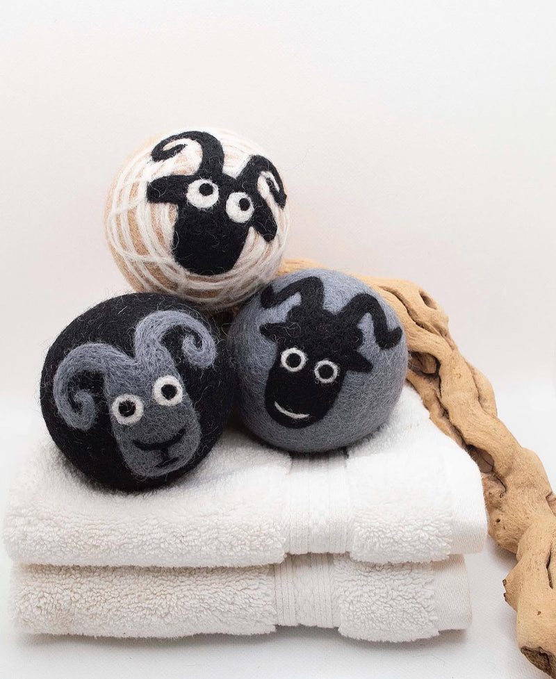 Three wool dryer balls with sheep faces rest on folded white towels next to a piece of driftwood.