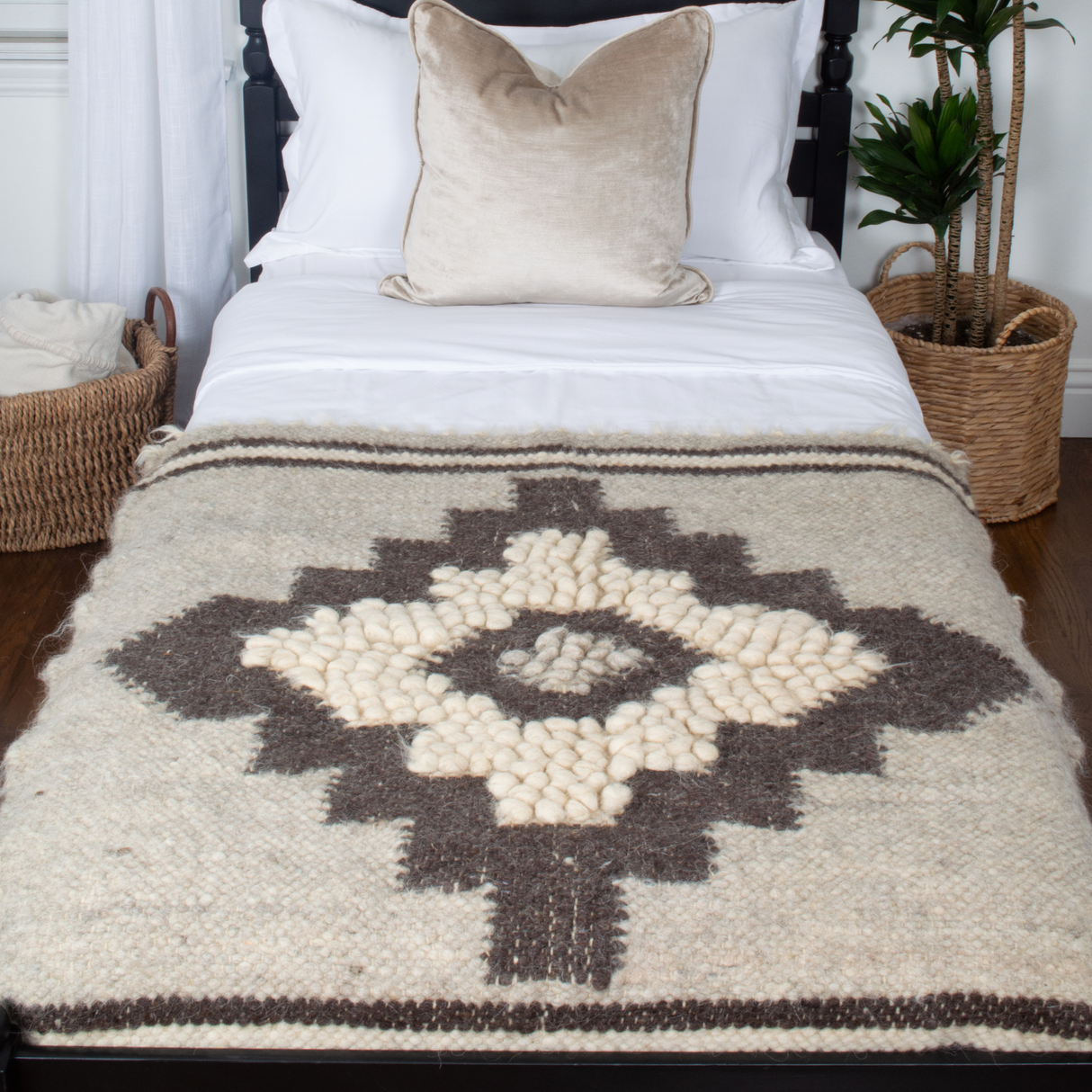 A neatly made bed features the Karaliene (Queen) Wool Wall Hanging with a rhombus-dot pattern above it, a beige pillow, and baskets beside the bed.