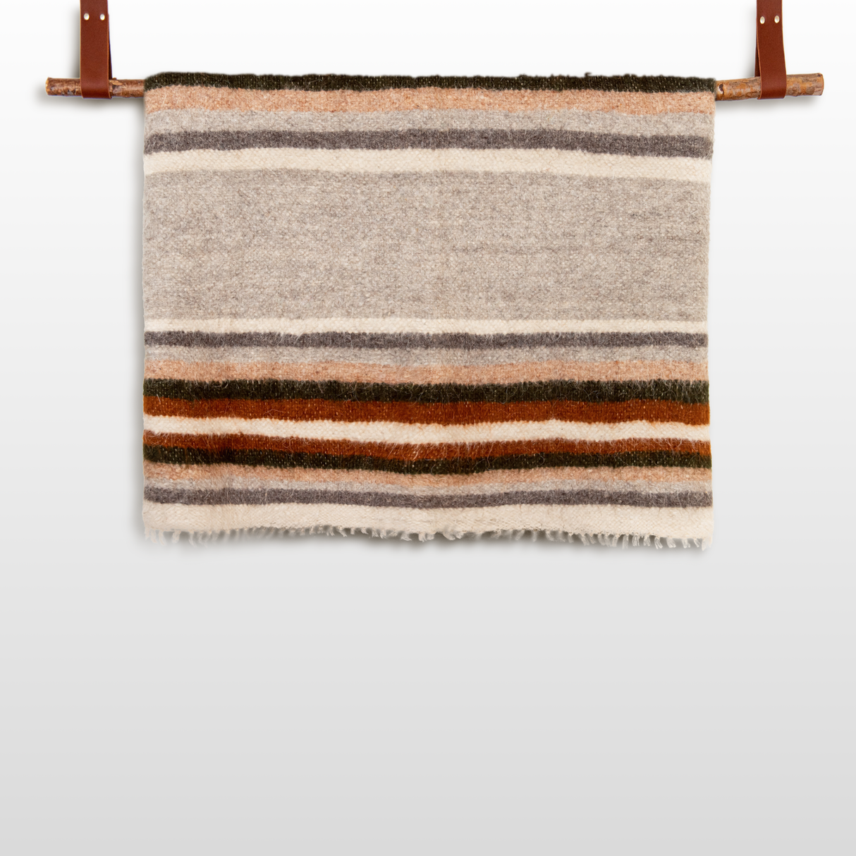 The Mudry (Wise) Wool Statement Baby Blanket, featuring brown, gray, orange, and cream stripes, hangs on a rod with leather straps.