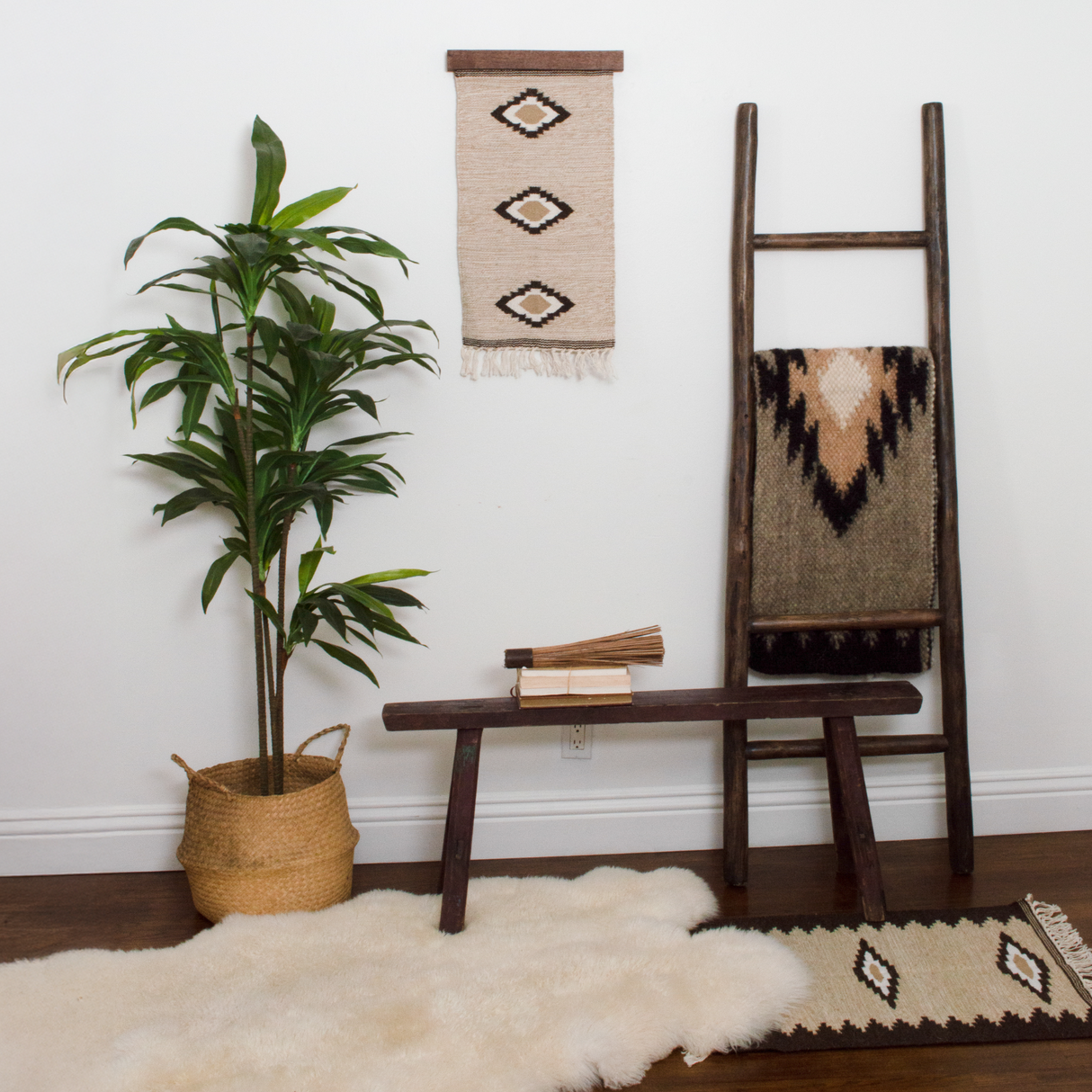 Boho decor features a potted plant, wooden bench, ladder with blanket, woven rug, and the Myr (Peace) Wool Wall Hanging—crafted from all-natural undyed yarn and inspired by traditional Ukrainian design.