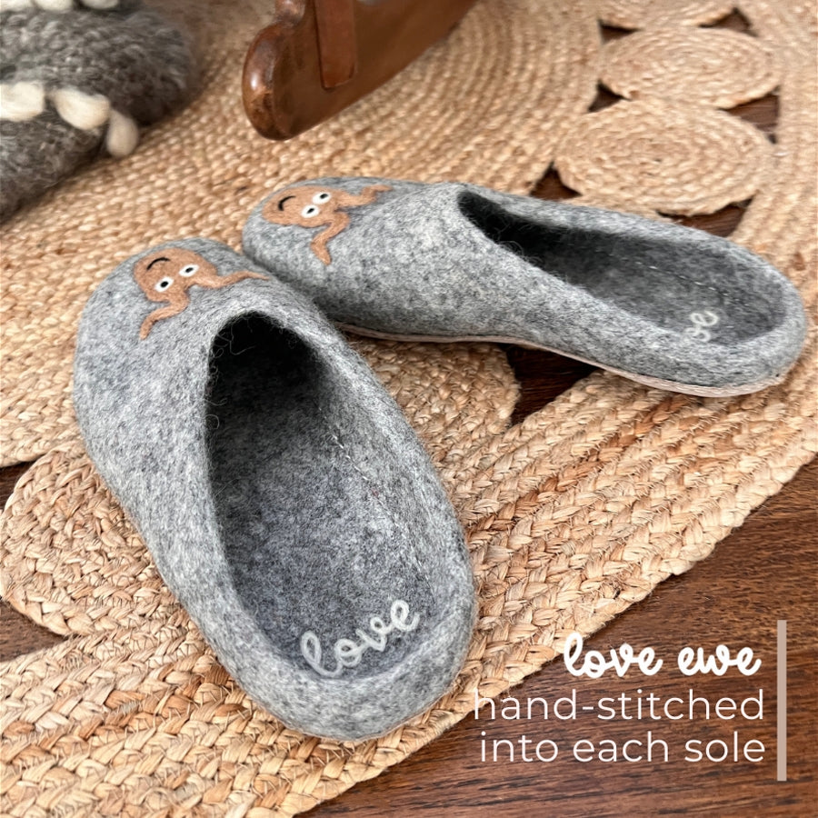 Love Ewe Hand-Felted Organic Wool Slippers for Men (Beau-G) feature a gray design with a cute sheep and "love" stitched on the sole, handcrafted in Nepal and pictured on a woven mat.