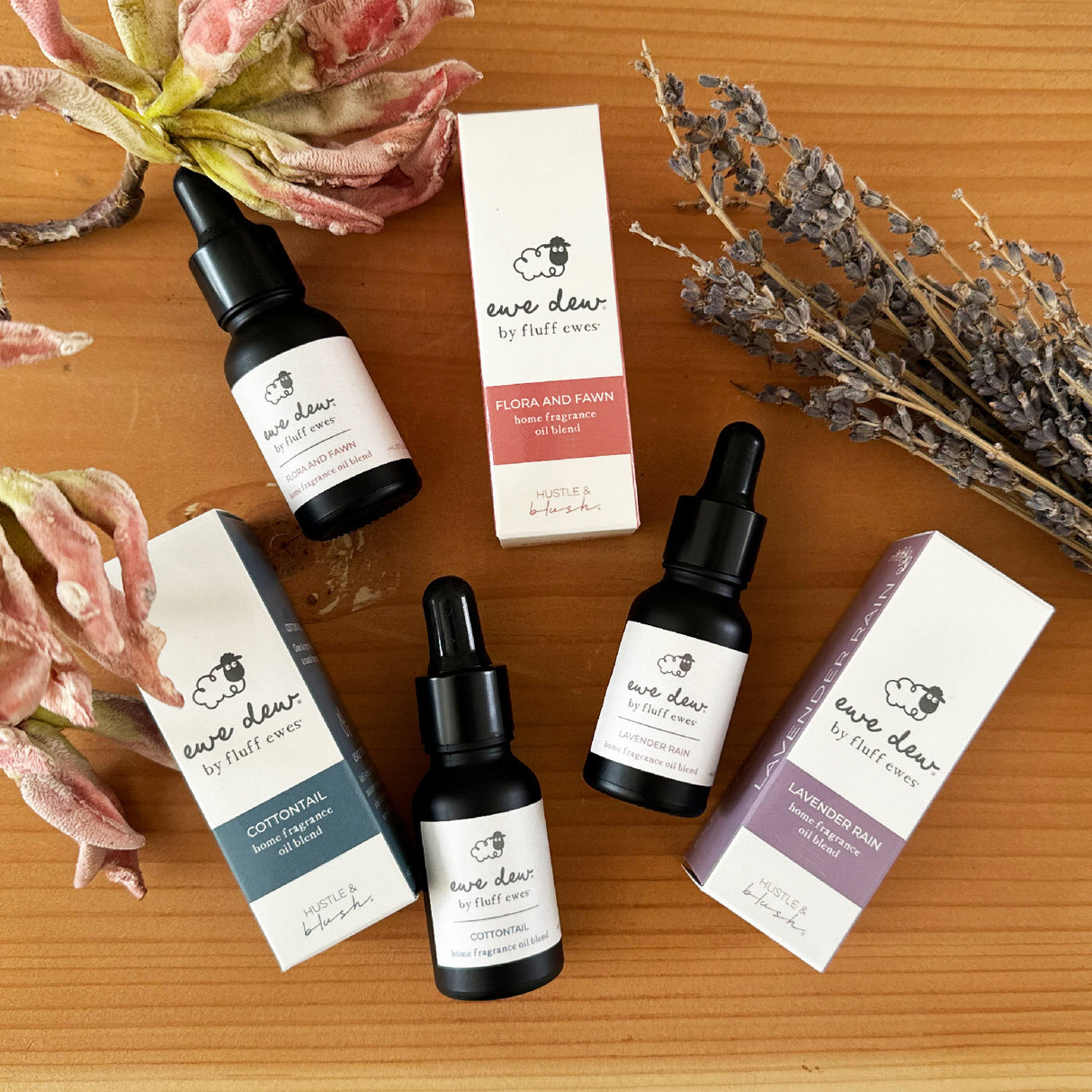 Fluff Ewes Premium XL Dryer Balls “Sheep in Heavenly Peace” 6 Pack Holiday Edition are displayed with dropper bottles, boxes, dried flowers, and lavender on a wooden surface.