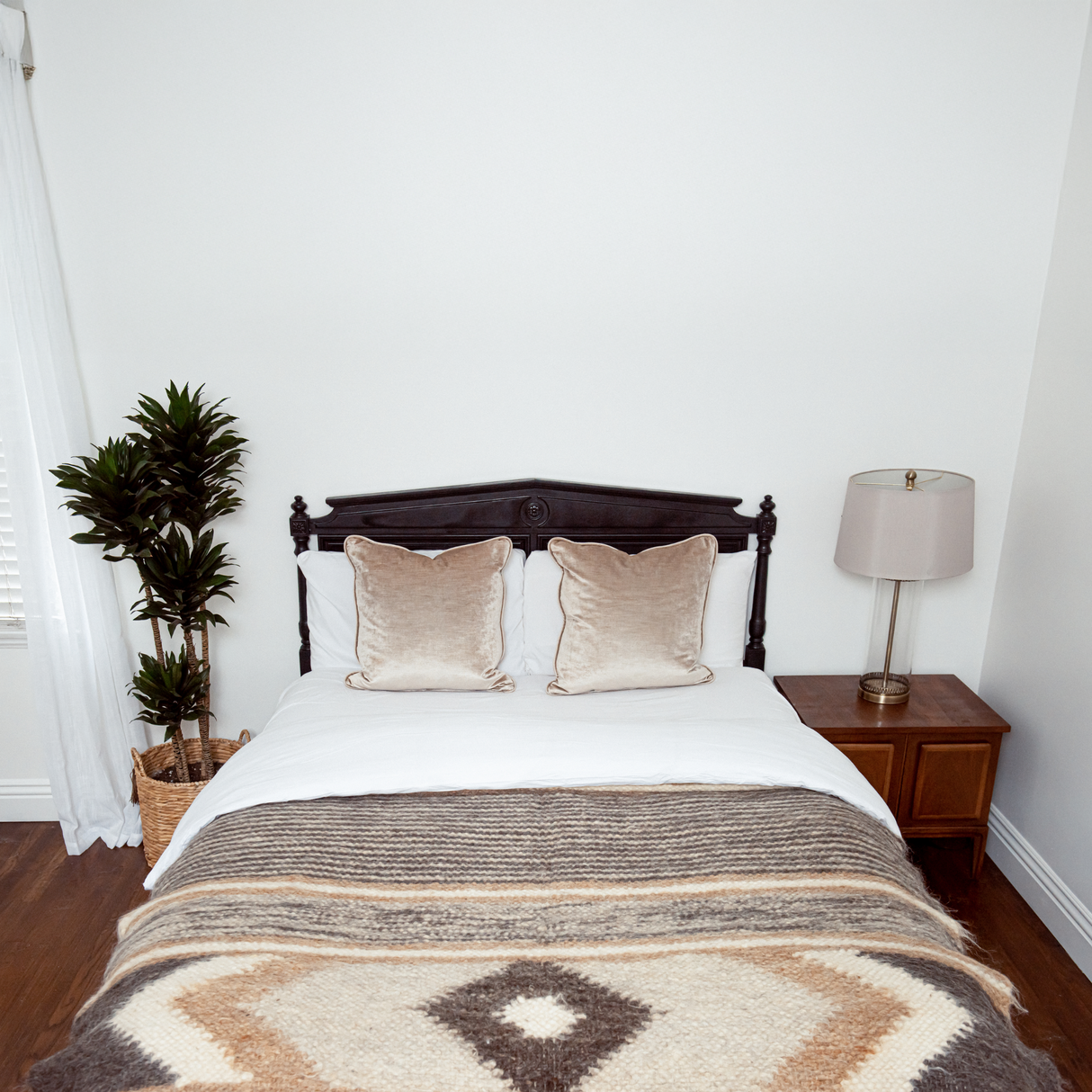 A neatly made bed with beige pillows topped by the Peremoha (Victory) Wool Statement Bed Blanket, alongside a potted plant and a lamp on a nightstand.