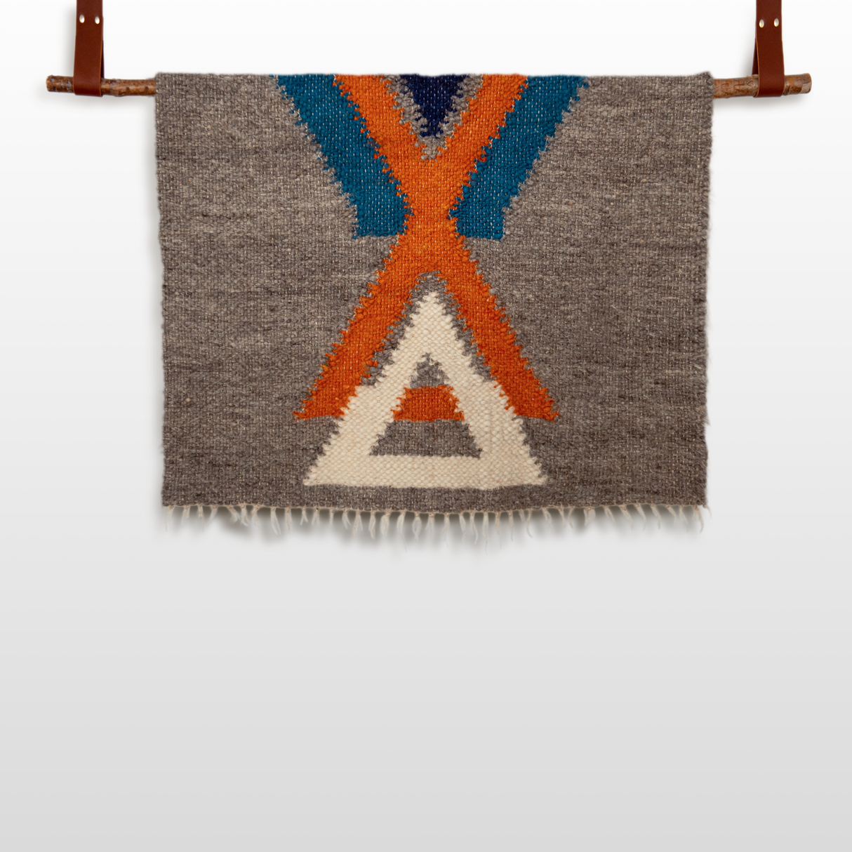 The Podyh (Breathe) Wool Statement Throw / Baby Blanket features handcrafted geometric patterns in orange, blue, and cream, and is displayed hanging from a wooden rod with leather straps.
