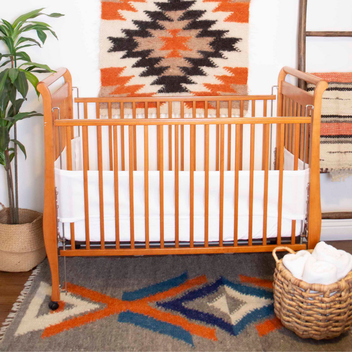 Wooden baby crib with white liner, southwestern rug, wall art, wicker basket, potted plant, and the Podyh (Breathe) Wool Statement Throw / Baby Blanket draped over the side.