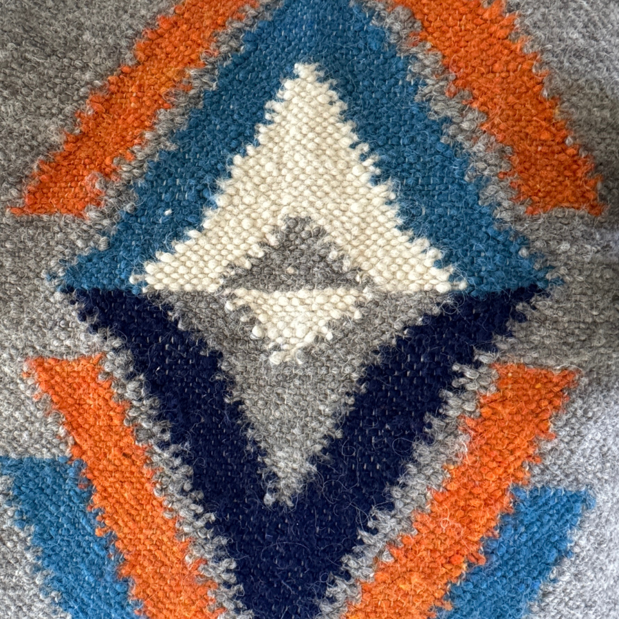 Close-up of the Podyh (Breathe) Wool Statement Throw / Baby Blanket, handcrafted with blue, orange, white, and navy geometric arrow patterns on a gray background.