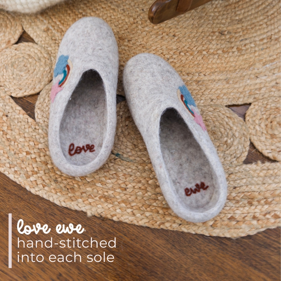 A pair of Love Ewe Hand-Felted Organic Wool Slippers for Women (Rainbow-Light), handmade in Nepal, rests on a woven rug.