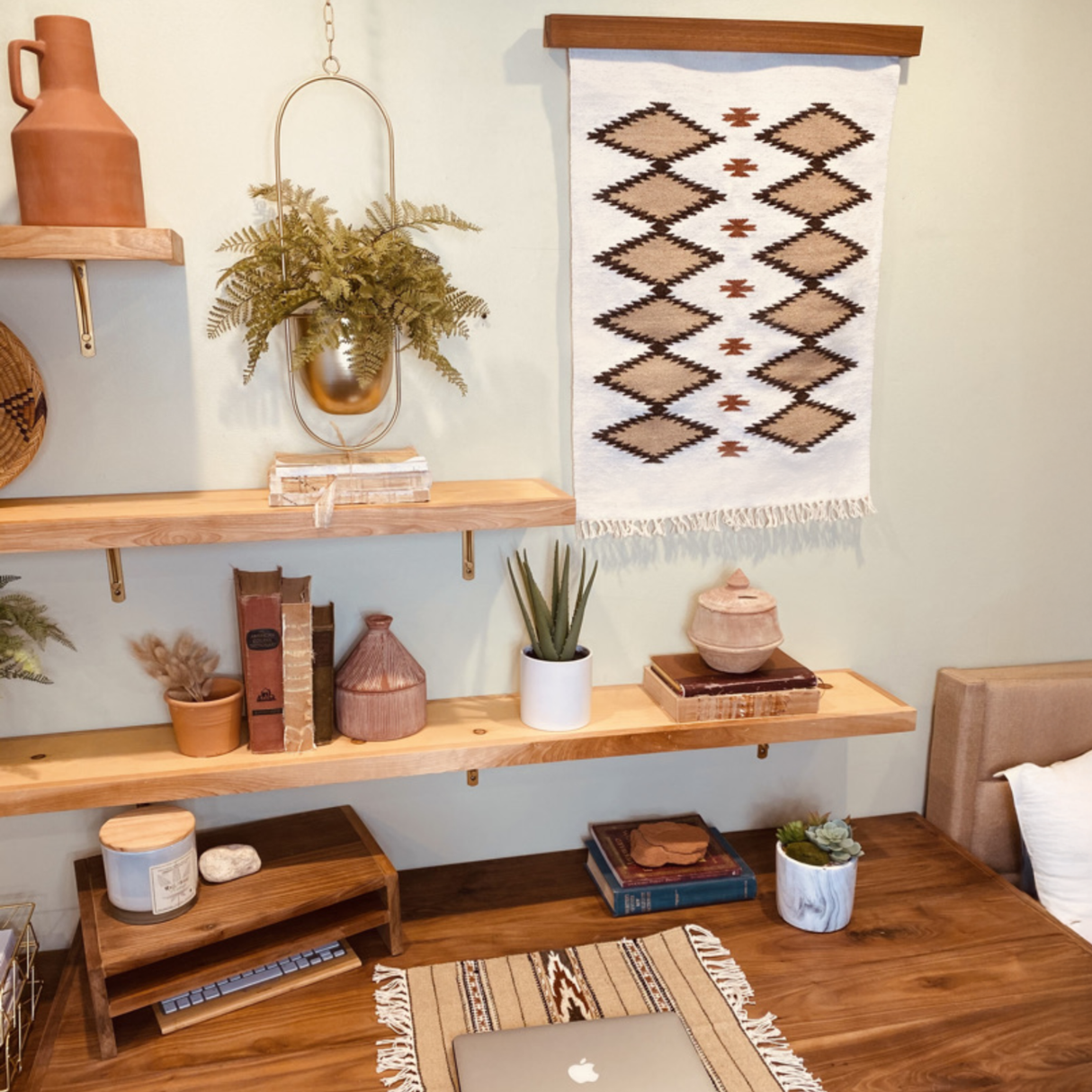 Wood desk with a laptop, shelves holding plants, books, pottery, and a Handmade in Ukraine Organic Natural 100% Sheep Wool Woven Rug Wall Hanging Decor above.