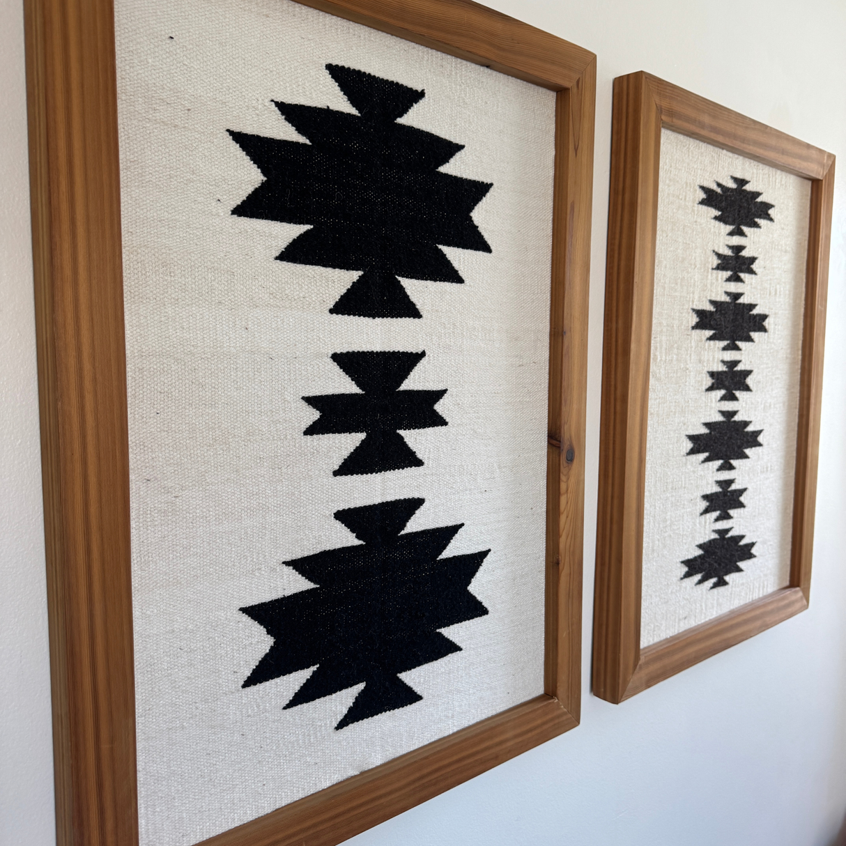 The Chysto (Pure) Wool Rug / Wall Hanging, displayed on a wood rug hanger, features bold black geometric designs on white. Its eco-friendly hanger adds a modern, sustainable touch to your wall for $240.