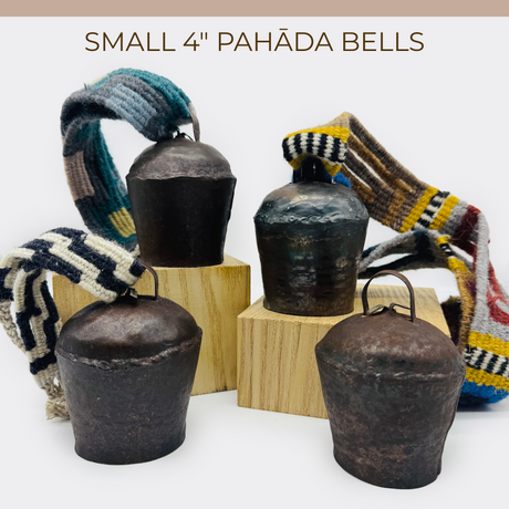 Four vintage handmade 4" Pahāḍa yak, goat & sheep's bells from the Himalayan mountains of Nepal and Tibet, each with colorful woven straps, displayed on wooden blocks. Perfect as Christmas ornaments, wreath decor, or for sound baths.