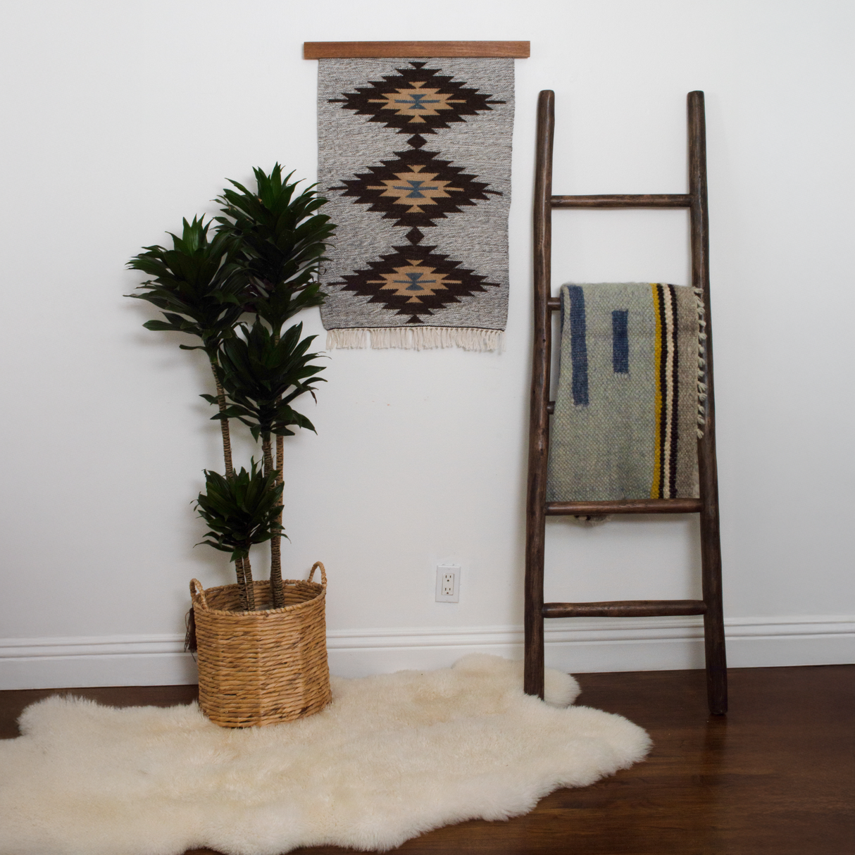 A potted plant, a Smilyv (Bold) Wool Rug / Wall Hanging, and a blanket on a wooden ladder decorate a cozy, minimalist room.