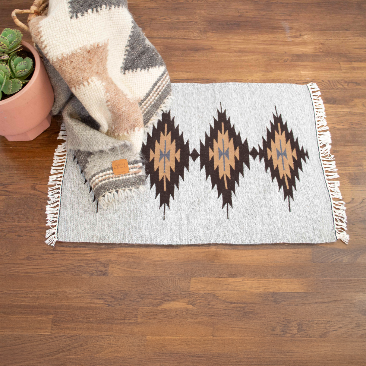 The Smilyv Wool Rug features gray neutral tones, geometric patterns, and fringed edges, bringing modern old-world style to any space as a rug or wall hanging.