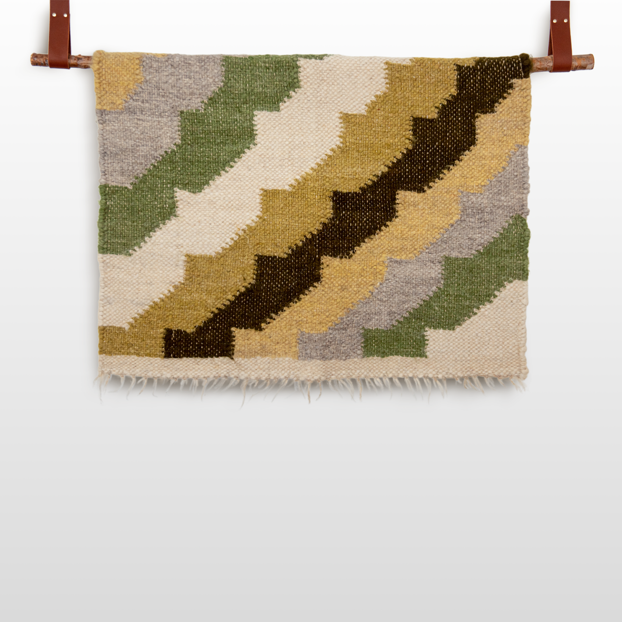 The Sontse (Sun) Wool Statement Throw / Baby Blanket is a handcrafted wool blanket with zigzag patterns in green, beige, brown, and cream, displayed hanging from two leather straps.