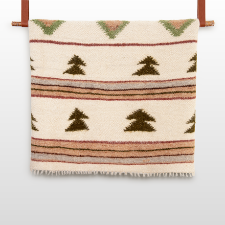 The Sosna (Pine) Wool Statement Bed Blanket features green, brown, and pink geometric patterns and hangs on a wooden rod—perfect for adding warmth and style to your mountain cabin.