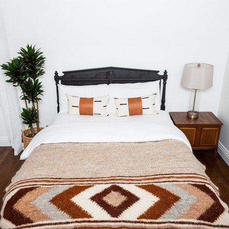 A bed with pillows, a lamp, and the Tkach (Weaver) Wool Statement Bed Blanket adds cozy charm to the room.