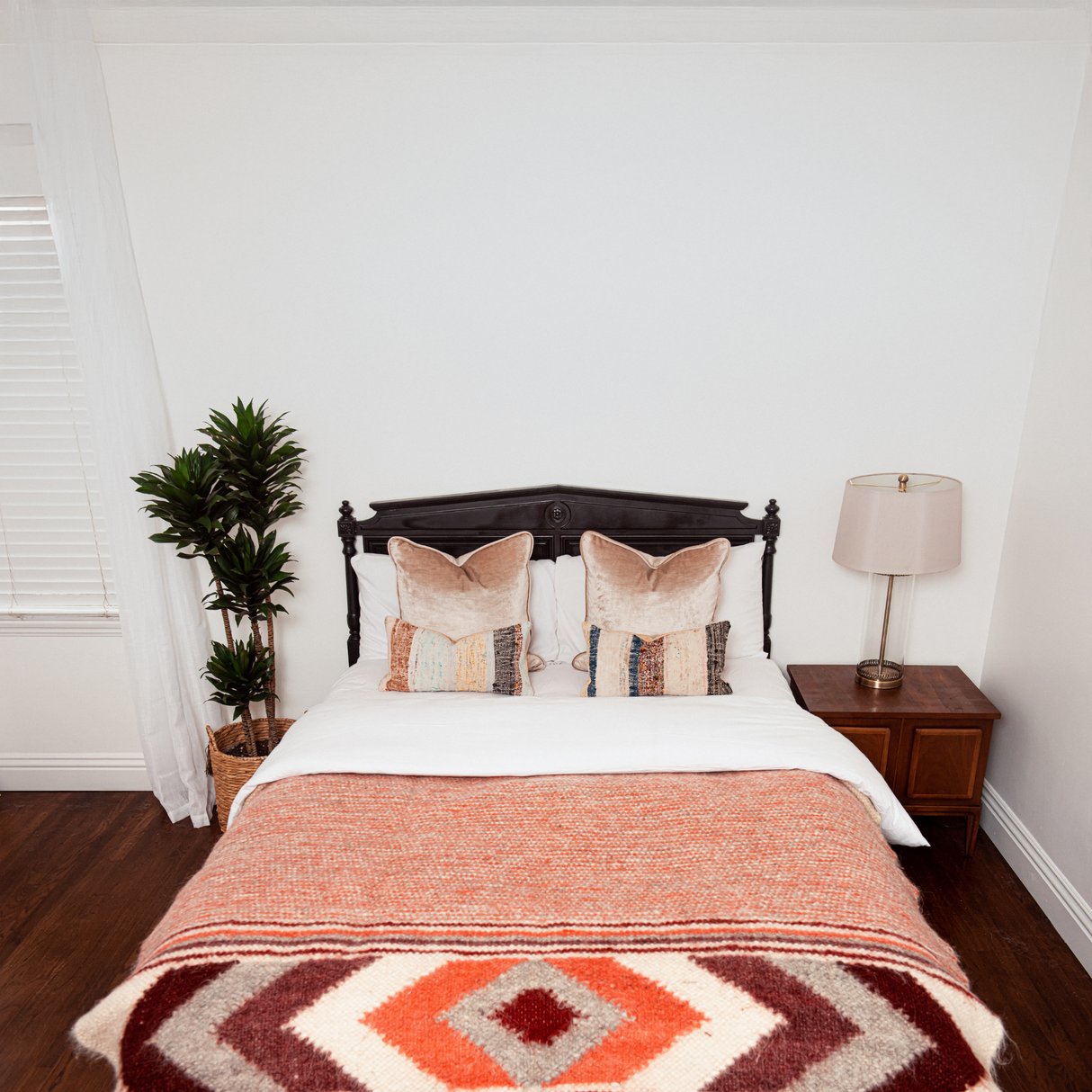 A neatly made bed features patterned pillows and the Tkach (Weaver) Wool Statement Bed Blanket, crafted from Carpathian sheep wool, alongside a plant and a lamp on wooden nightstands.