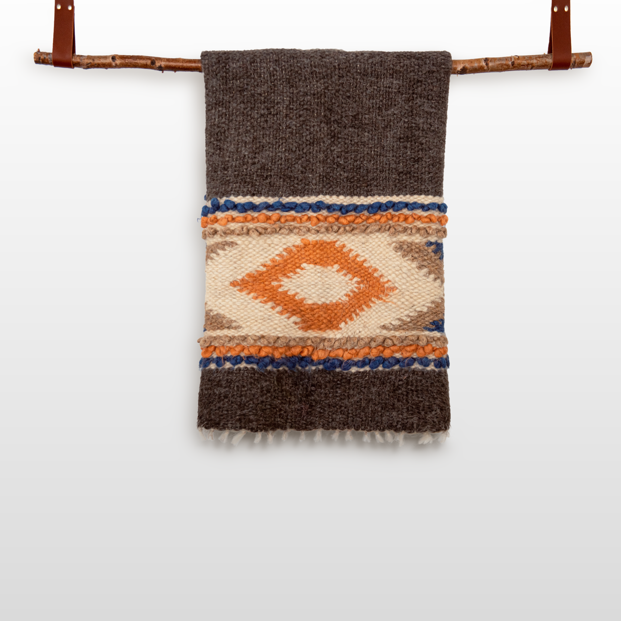 The Tkach (Weaver) Wool Statement Bed Blanket, featuring geometric patterns, can be draped over a wooden branch with leather straps to create a striking woven wall hanging.