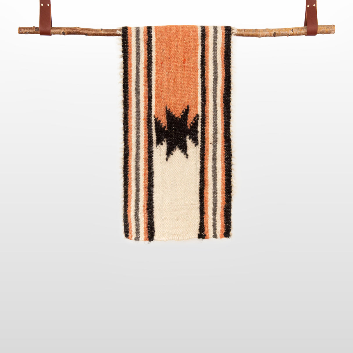 The Opora (Pillar) Wool Bed/Couch Runner, handcrafted from Carpathian sheep wool, features black star designs with orange and black stripes and hangs from a wooden rod with leather straps—ideal as a distinctive bed runner.