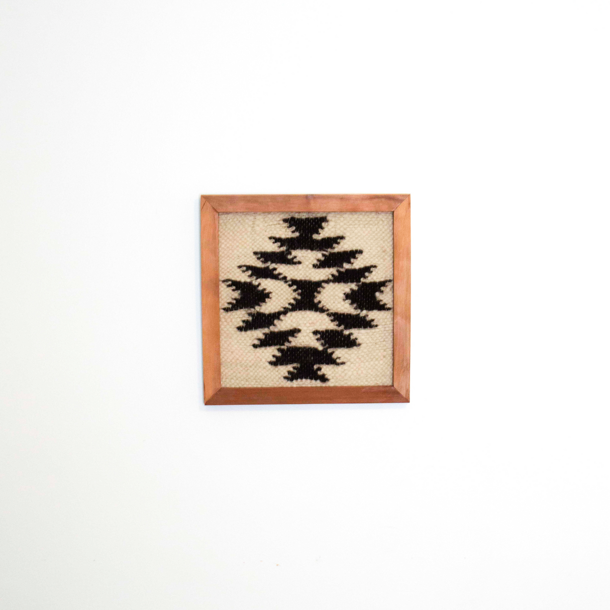 The Vira (Faith) Wool Framed Wall Art features a black geometric pattern on undyed sheep’s wool, beautifully set in a cedar frame and displayed on a white wall.