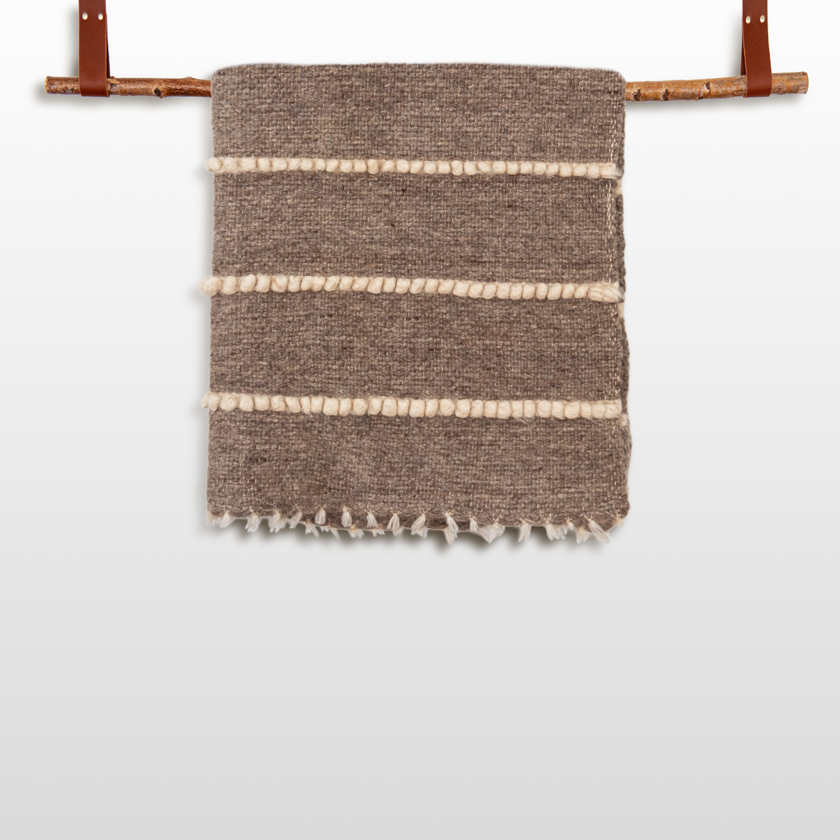 The Vivtsi (Sheep) Wool Statement Throw / Baby Blanket features a brown textured design with white horizontal stripes, hanging on a wooden rod with leather straps—ideal as a stylish accent for cozy spaces.
