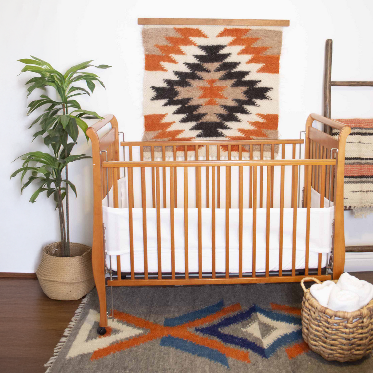 A cozy nursery features a wooden crib with white bedding, southwestern decor, a potted plant, and the Zirka (Star) Wool Wall Hanging, handcrafted and inspired by the Ukrainian star motif.