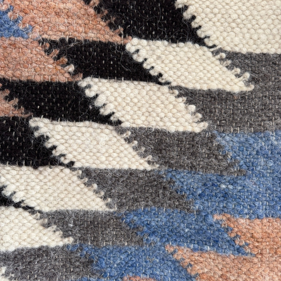 Close-up of the Zirka (Star) Wool Statement Throw / Baby Blanket, featuring a handcrafted geometric pattern in black, white, gray, blue, and pinkish-brown—an eye-catching accent for any space.