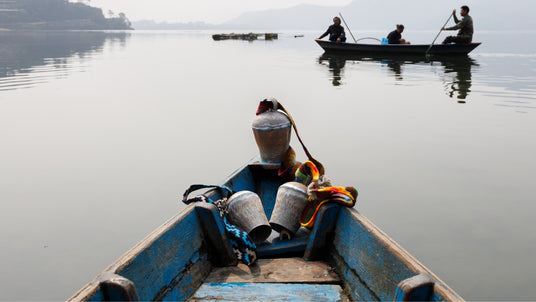 View from a blue wooden boat on calm water, with metal containers, and another boat with people in the distance.