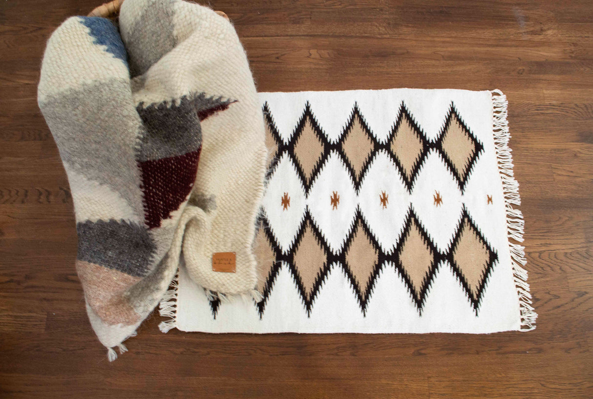 A Handmade in Ukraine Organic Natural 100% Sheep Wool Woven Rug Wall Hanging Decor rests by a folded multicolored knit blanket on a wooden floor.