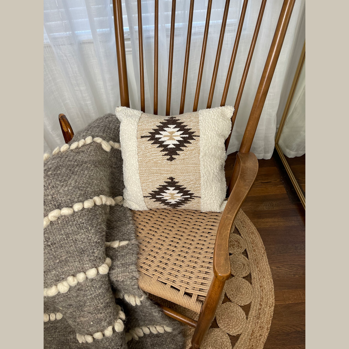 Wooden rocking chair with a woven seat, featuring the Handwoven Chitki (Crisp) Pillow and a chunky knit blanket draped over the arm.