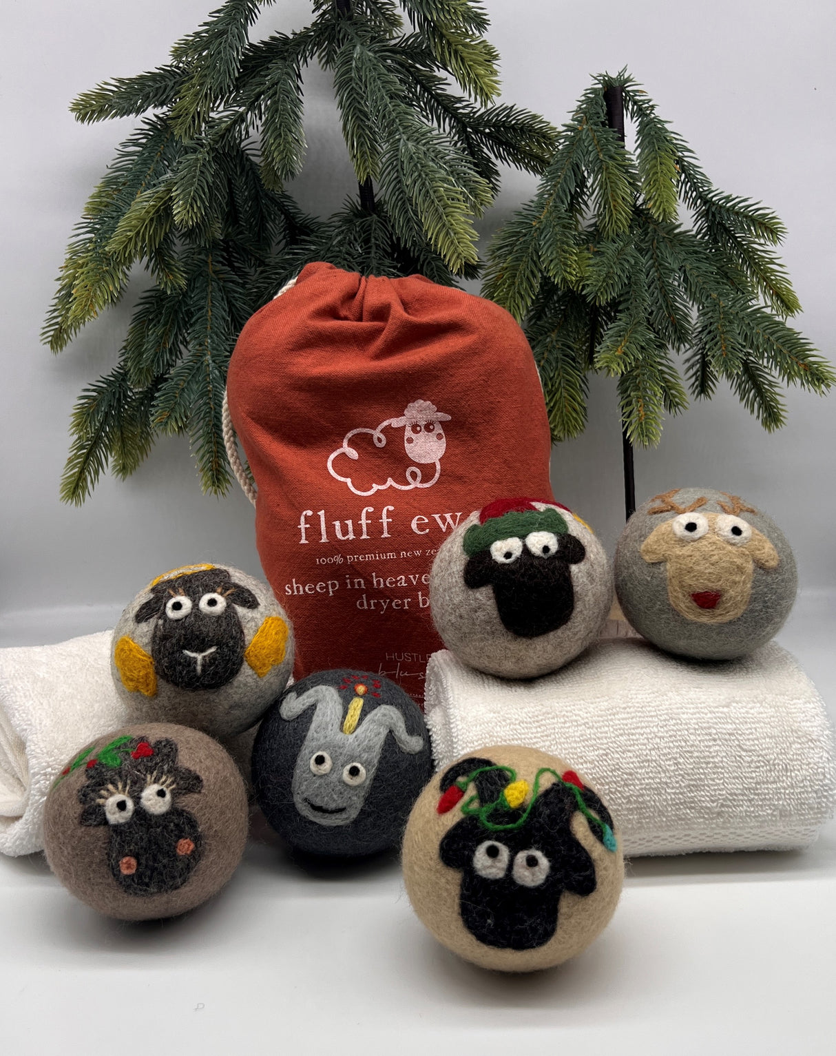 The Fluff Ewes Premium XL Dryer Balls "Sheep in Heavenly Peace" Holiday 6 Pack, featuring eco-friendly wool balls with animal faces and a red bag, offers a natural fabric softener alternative.