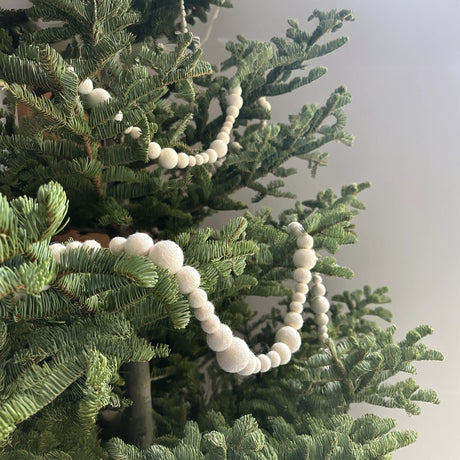 Close-up of a green Christmas tree decorated with a white pom-pom garland, against a plain background.