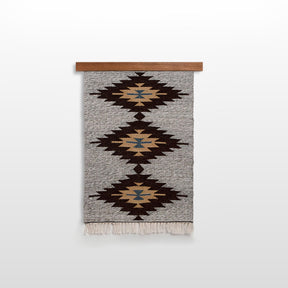 The Smilyv (Bold) Wool Rug / Wall Hanging features geometric patterns in brown, black, beige, and blue on a wooden rod, adding modern neutral charm to your décor as both a wall hanging and a rug.