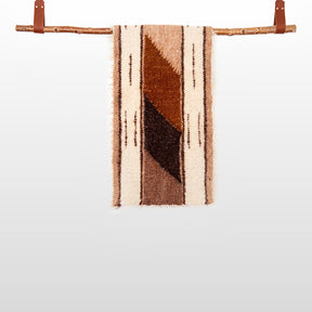 The Tak (Yes) Wool Bed / Couch Runner, featuring handcrafted geometric brown patterns, is displayed hanging from a wooden branch against a plain background.