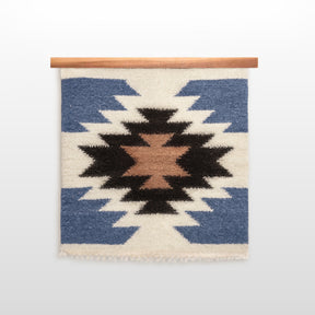 The Zirka (Star) Wool Wall Hanging is handcrafted from Carpathian sheep wool with blue, white, brown, and black geometric patterns, and displayed on a wooden rod.
