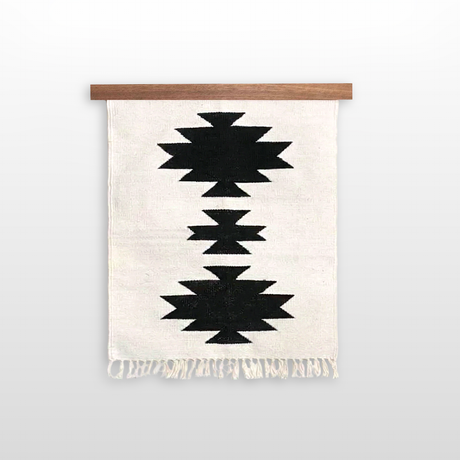 The Chysto (Pure) Wool Rug / Wall Hanging, made from organic Carpathian wool, features three black geometric patterns and fringed ends, and comes with a wooden rug hanger.
