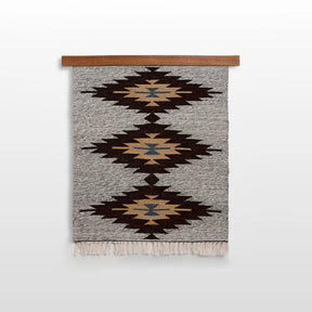 Handmade in Ukraine, this wall hanging is woven from 100% organic sheep wool and features three diamond patterns in brown, gold, and blue with fringe at the bottom.
