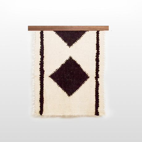 The Korysno (Helpful) Wool Bed/Couch Runner is woven from organic Carpathian wool with two black diamonds on a white background and comes on a wooden rod—an elegant, sustainable accent for your home.
