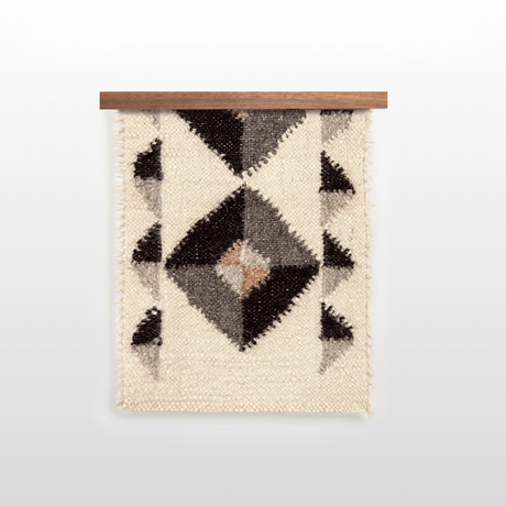The Iskara (Spark) Wool Bed / Couch Runner features black, gray, and brown geometric diamond shapes on a cream background, mounted on wood for a stylish woven display.