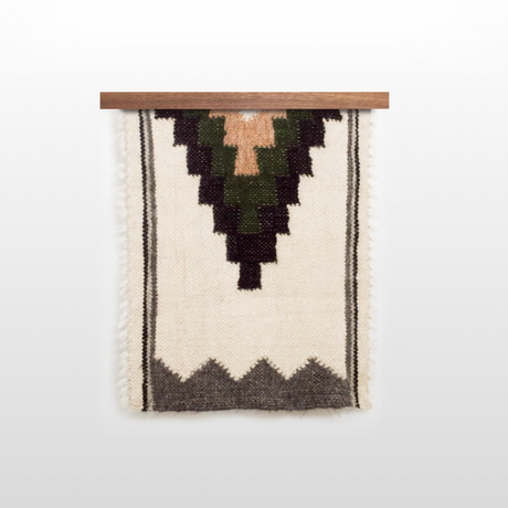 The Myr (Peace) Wool Bed / Couch Runner - Style A features geometric black, green, and tan patterns on a cream base, hung on a wooden rod—perfect for sustainable home decor inspired by handwoven design.