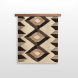 The Svitlo (Bright) Wool Wall Hanging features geometric patterns in earth tones, crafted from organic Carpathian wool, and is displayed hanging on a wooden rod against a white background.
