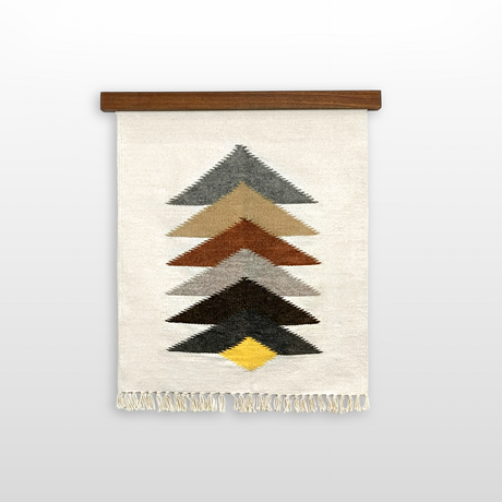 The Strilka (Arrow) Wool Rug/Wall Hanging features handwoven zigzag arrows in gray, brown, black, and yellow on cream organic Carpathian wool, and hangs from a wooden rod.